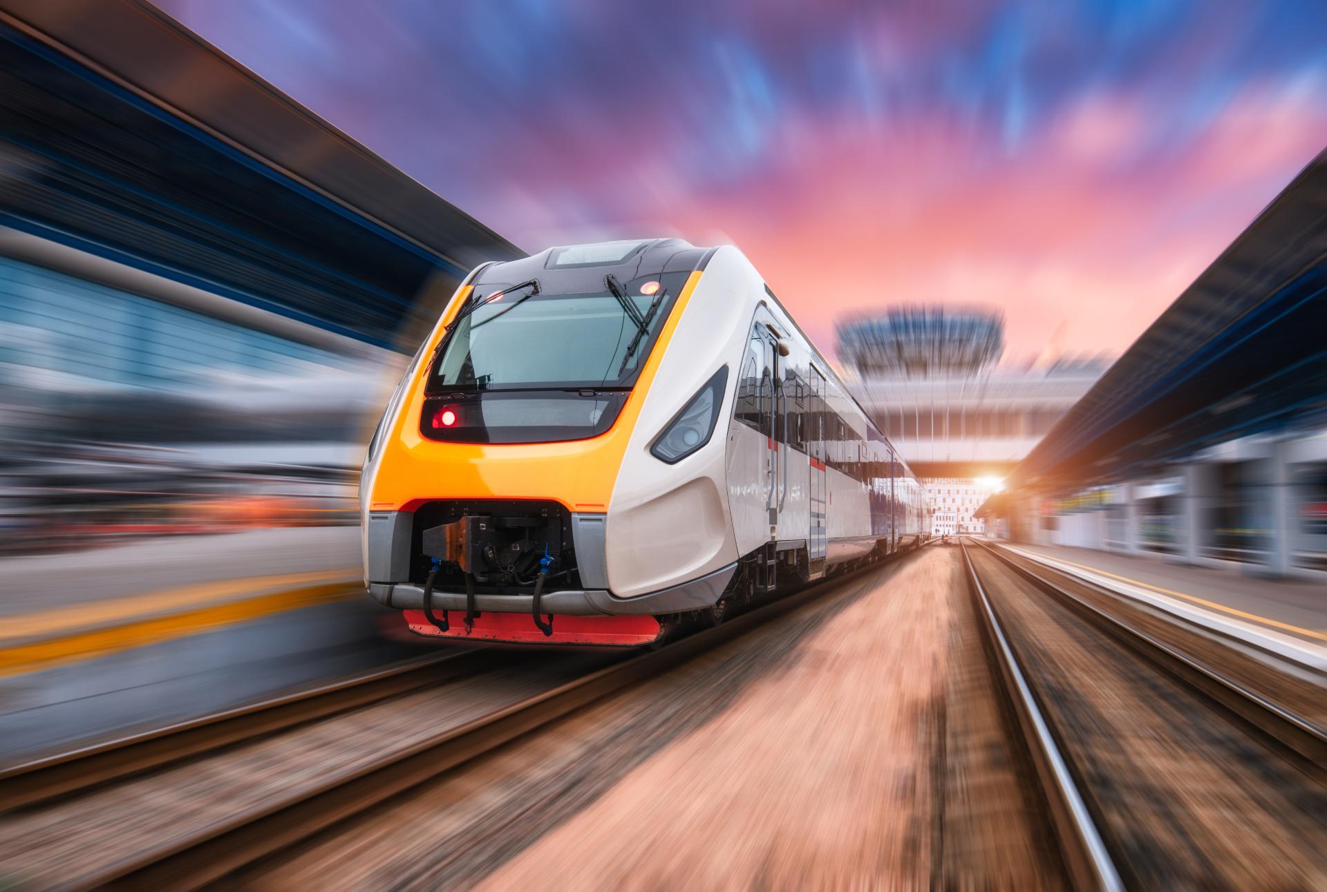 High speed train in motion on the railway station at sunset. Fast moving modern passenger train on railway platform. Railroad with motion blur effect. Commercial transportation. Front view. Concept